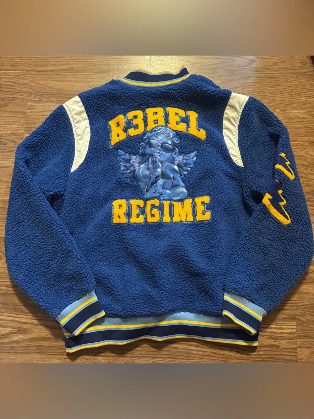 Soft  blue sherpa jacket with bold yellow 'Rebel Regime' lettering and angel